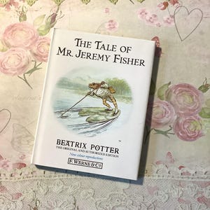 Peut inclure: Un livre intitulé "The Tale of Mr. Jeremy Fisher" de Beatrix Potter. La couverture présente une illustration d'une grenouille en train de pêcher. Il s'agit d'une édition originale et autorisée avec de nouvelles reproductions en couleur.