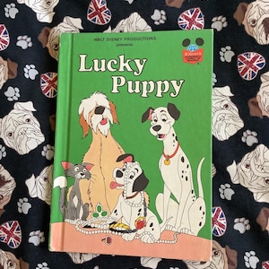 May include: A green hardcover book titled Lucky Puppy by Walt Disney Productions. The cover features a cartoon illustration of a cat, a shaggy brown dog, a small spotted puppy wearing a pearl necklace, and a dalmatian dog with a yellow collar.