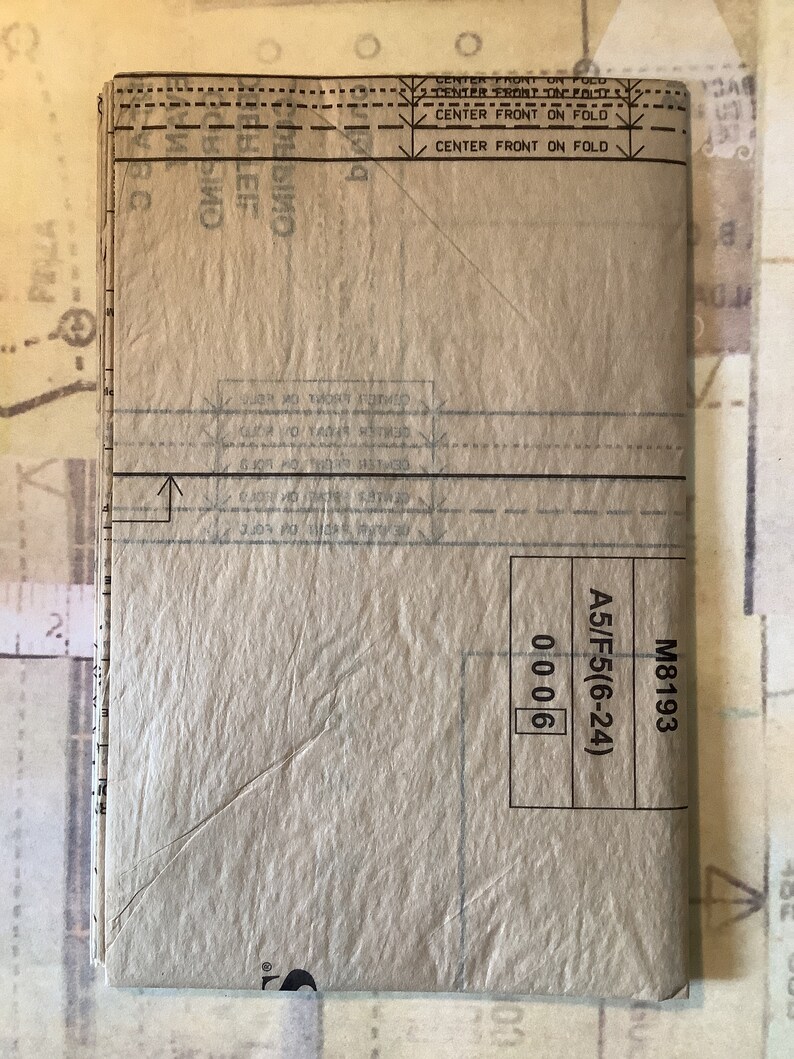 May include: A brown paper pattern with instructions for sewing a garment. The pattern is labeled "M8193 A5/F5(6-24) 0006".