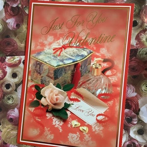 May include: A Valentine's Day card with a red and gold border, featuring a decorative box, perfume bottle, and a rose. The card reads "Just For You Valentine" and includes a tag that says "Love You". Two gold heart-shaped embellishments are also visible.
