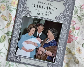 Może przedstawiać: Szara książka z srebrną ramką i tytułem "Princess Margaret Wife and Mother" autorstwa Patricka W. Montague-Smitha. Okładka przedstawia czarno-białe zdjęcie księżnej Małgorzaty trzymającej dziecko z mężem i inną kobietą stojącą za nimi.