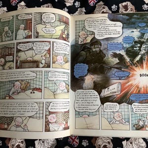 Puede incluir: Un libro de historietas abierto con paneles de c&oacute;mic. Las ilustraciones son de estilo vintage, con una paleta de colores apagados. Los paneles representan escenas con personajes en varios escenarios, incluyendo un dormitorio y una escena de guerra. Las burbujas de di&aacute;logo contienen texto.