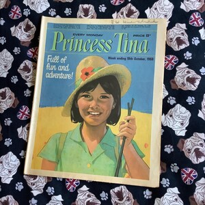 以下が含まれることがあります： 緑のシャツと麦わら帽子をかぶった若い女の子が、杖を持っている、ビンテージ雑誌の表紙。雑誌のタイトルは「プリンセス・ティナ」で、タイトルの下には「Full of fun and adventure!」という文字が印刷されている。表紙には、「Every Monday, Price 8p, Week ending 19th October, 1968.」という文字も書かれている。