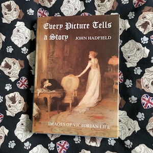 May include: A hardcover book titled "Every Picture Tells a Story" by John Hadfield, with an image of Victorian life. The book is set against a black background with a pattern of white pugs, paw prints, and Union Jack flags.