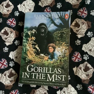 May include: A paperback book cover with a photo of a gorilla in a jungle setting. The title is "Gorillas in the Mist" and the author is Dian Fossey. The book cover also mentions that the book is the basis for a film starring Sigourney Weaver and Bryan Brown.