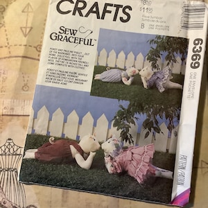 May include: A McCall's Crafts sewing pattern titled "Sew Graceful" featuring illustrations of piglet dolls. The pattern includes instructions for making the dolls, which are 19 inches tall and come with clothes. The pattern is in an envelope.