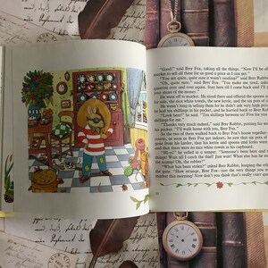 Op de afbeelding: Een kleurrijke illustratie van een vos en een konijn in een keukenomgeving. De vos houdt een mand met goederen vast, waaronder een witte handdoek, een waterkoker en potten jam. Het konijn zit op een stoel en kijkt naar de vos. De tekst in de afbeelding luidt: "Goed!" zei Brer Vos, nam alle dingen. "Nu ga ik naar de markt om dit alles voor de best mogelijke prijs te verkopen."