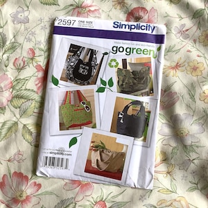 May include: Simplicity sewing pattern number 2597, "go green" with one size, featuring five different tote bag designs. The bags are made from various fabrics, including camouflage, floral, and solid colors.