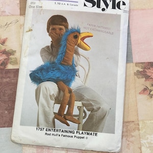 May include: A vintage sewing pattern for a puppet, depicting a blue and brown bird. The pattern is titled "1757 ENTERTAINING PLAYMATE" and includes the text "Style" and "PAPER PATTERNS NOT EXCHANGEABLE". The pattern is one size and priced at 1.10 S.A. & Canada.