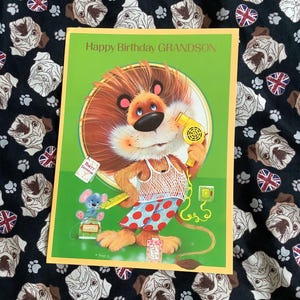 May include: A birthday card featuring a cartoon lion with a yellow hairdryer. The lion is dressed in a vest and red polka dot shorts. The card has the text "Happy Birthday GRANDSON" on a green background.