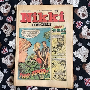 May include: A vintage copy of "Nikki for Girls" comic, dated August 9th, 1986, with a cover featuring a comic strip. The comic strip is titled "Two Timer!" and includes illustrations. The background is a black fabric with white dog faces and Union Jacks.