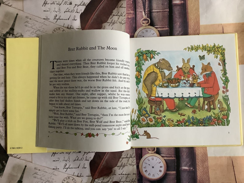 Op de afbeelding: Een illustratie uit een kinderboek met Brer Rabbit, Brer Fox en Brer Bear die aan een tafel zitten met een kom eten en drinken. De illustratie is omringd door een groene rand met bloemen en vlinders.