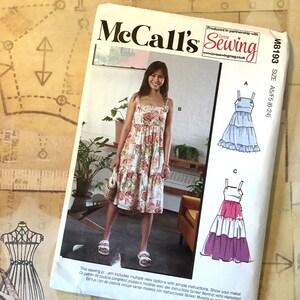May include: McCall's Sewing pattern M8193, size A5/F5 (6-24), featuring three different styles of dresses. The first dress is a floral print, the second is a light blue tiered dress, and the third is a pink, white, and purple tiered dress. The pattern includes simple instructions and multiple view options.