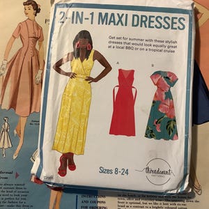 May include: A vintage sewing pattern for 2-in-1 maxi dresses. The pattern packet features illustrations of the dresses, including a yellow floral print dress, a red dress, and a teal floral dress. The packet also includes the text "Sizes 8-24".