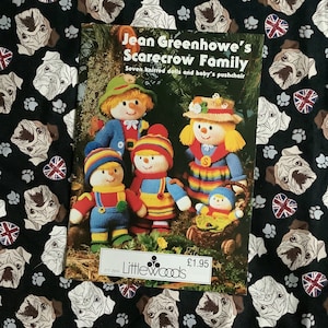 May include: A book cover with the title "Jean Greenhowe's Scarecrow Family" and the text "Seven knitted dolls and baby's pushchair". The cover features a colorful illustration of seven knitted scarecrows, including a baby scarecrow in a basket.