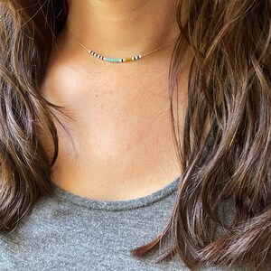 May include: A delicate gold chain necklace with small, colorful beads. The beads are white, black, turquoise, and yellow.