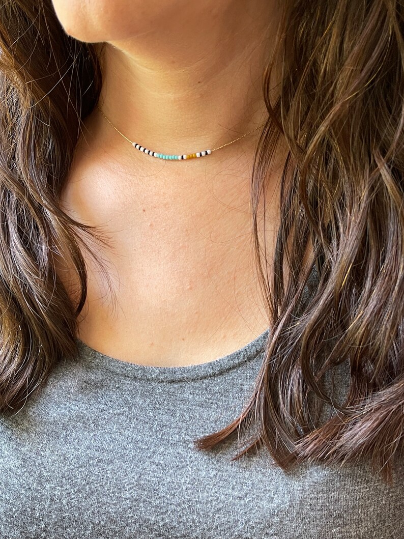 May include: A delicate gold chain necklace with small, colorful beads. The beads are white, black, turquoise, and yellow.
