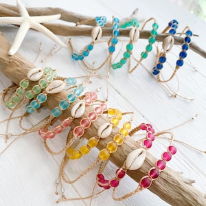 May include: A set of colorful bracelets made with glass beads and shell charms. The bracelets are strung on a natural cord and come in a variety of colors, including blue, green, pink, yellow, and red.