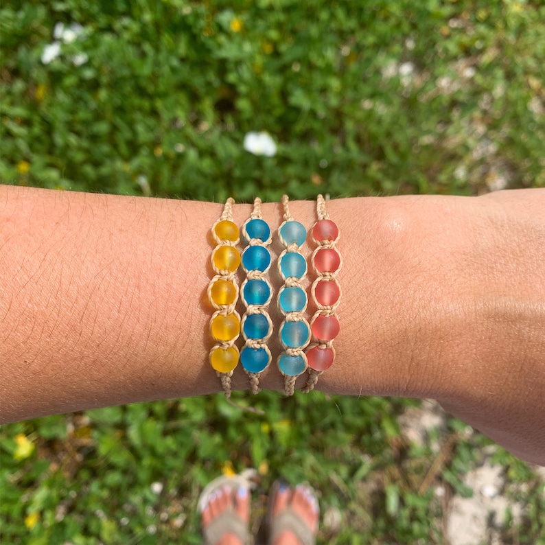 May include: Four bracelets with different colored glass beads. The bracelets are made of natural twine and feature yellow, blue, and pink beads.