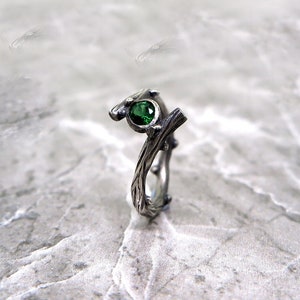 May include: A silver ring with a green gemstone set in a twig-like design.