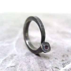 May include: A silver ring with a single, small, red gemstone set into the band.
