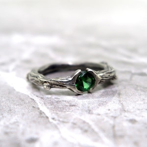 May include: A silver ring with a green gemstone set in a twig-like band.