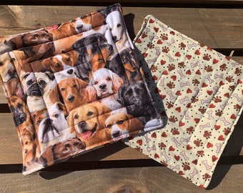 May include: Two quilted pot holders. One features a pattern of various dog breeds, the other has a pattern of red hearts, paw prints, and bones on a beige background.