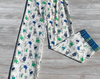 May include: White pajama pants with a blue, green, and gray dog print. The pants have a plaid trim at the bottom.