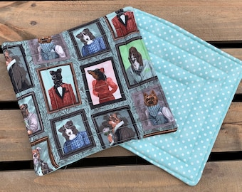 May include: Two quilted pot holders. One is a light blue fabric with white polka dots. The other is a light blue fabric with a pattern of dogs in framed portraits wearing clothing.