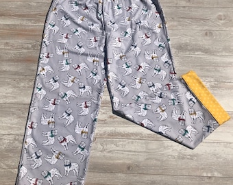 May include: Gray pajama pants with a white dog print and yellow trim. The dogs are wearing colorful scarves.