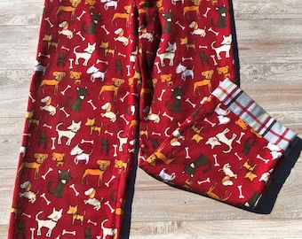 May include: Red pajama pants with a repeating pattern of various dog breeds and white bone shapes. The pants have a plaid cuff at the ankle. The elastic waistband is visible.