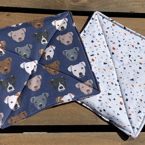 May include: Two blue and white pot holders. One has a pattern of white dogs on a blue background. The other has a white background with a terrazzo pattern of blue, orange, and purple.
