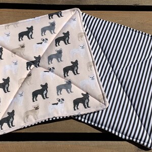 May include: Two square pot holders. One has a beige background with repeating French bulldog illustrations in black, grey, and white. The other has a black and white striped pattern. Both are quilted.