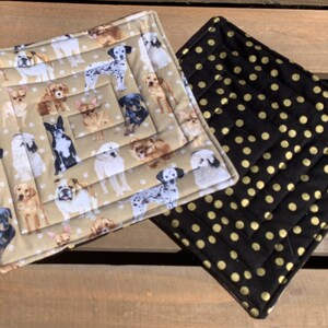 May include: Two quilted pot holders. One is beige with a pattern of dogs and paw prints. The other is black with gold polka dots.