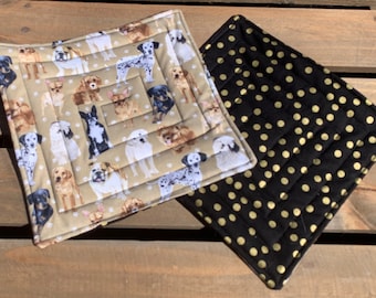 May include: Two quilted pot holders. One is beige with a pattern of dogs and paw prints. The other is black with gold polka dots.