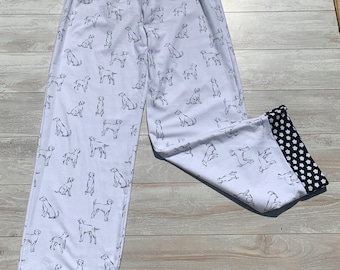 May include: White pajama pants with a black and white dog print. The pants have a black elastic waistband and black and white polka dot trim at the bottom.