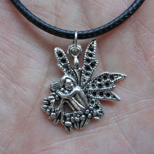May include: A silver pendant necklace with a fairy design. The fairy is sitting on a flower with wings spread out. The necklace is on a black cord.