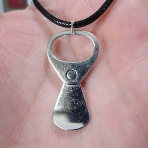 May include: A silver pull tab necklace with a black cord. The pull tab is shaped like a bottle opener.
