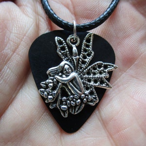 May include: A black guitar pick necklace with a silver fairy charm. The fairy is holding a flower and has delicate wings.