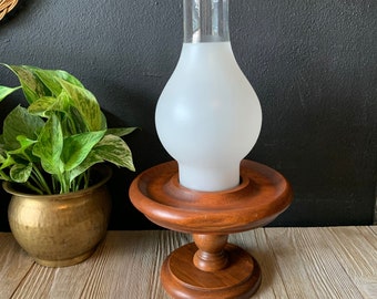 May include: A wooden candle holder with a frosted glass hurricane lamp. The holder has a round base and a pedestal design.