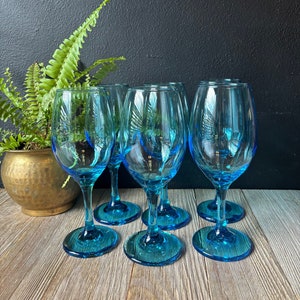 May include: Six turquoise blue wine glasses on a wooden surface. The glasses are clear and have a slight blue tint.