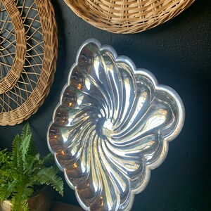 May include: A silver, swirl-shaped serving dish with a scalloped edge. The dish is made of metal and has a shiny, reflective surface.