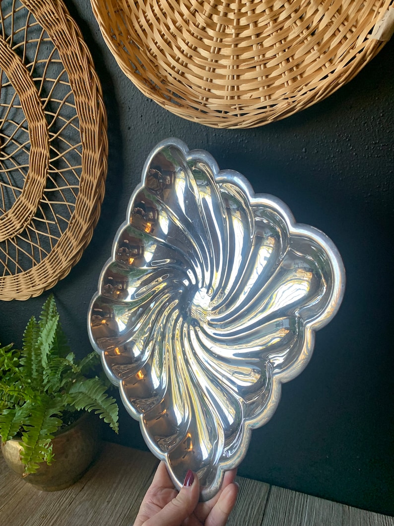 May include: A silver, swirl-shaped serving dish with a scalloped edge. The dish is made of metal and has a shiny, reflective surface.
