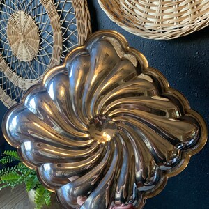 May include: A silver, swirl-shaped serving dish with a scalloped edge. The dish is made of metal and has a shiny finish.