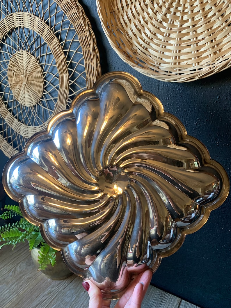 May include: A silver, swirl-shaped serving dish with a scalloped edge. The dish is made of metal and has a shiny finish.