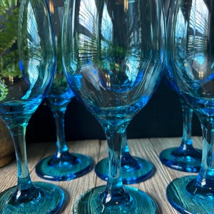 May include: Set of six blue glass wine glasses with a textured design. The glasses are clear and have a round bowl and a long stem.