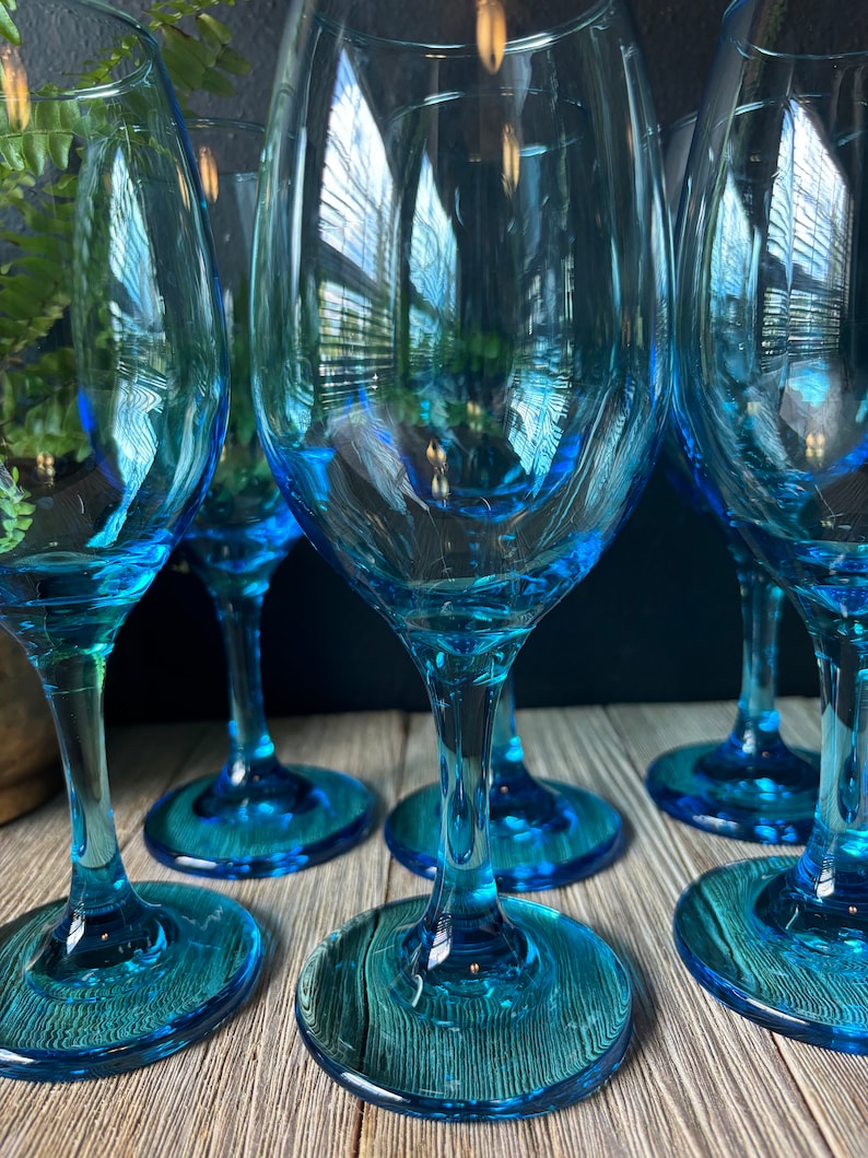 May include: Set of six blue glass wine glasses with a textured design. The glasses are clear and have a round bowl and a long stem.