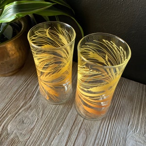 May include: Two clear glass drinking glasses with a yellow and orange wheat design.