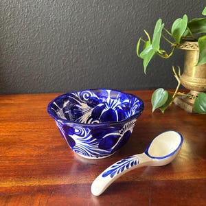 May include: A blue and white ceramic bowl and spoon set. The bowl has a floral design with blue and white accents. The spoon has a curved handle and a small bowl. The set is on a wooden surface.