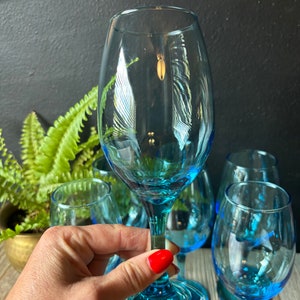May include: Set of six blue glass wine glasses. The glasses have a clear, transparent body and a blue base. The glasses are arranged on a wooden surface.